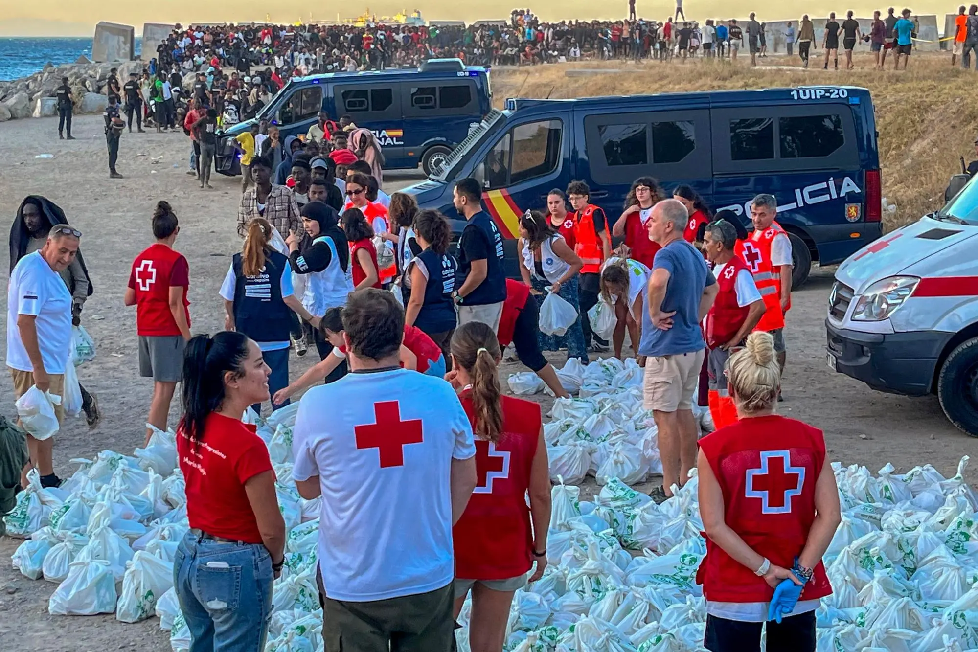 epa13150618 Red Cross personnel distribute food to migrants at El Trampolin beach in Ceuta, Spain, 04 August 2026. According to Spanish officials, around 2,500 migrants remain in Ceuta following last week's massive border rush from Morocco, with many living in overcrowded reception centers or sleeping outdoors on beaches and in parks. EPA/REDUAN