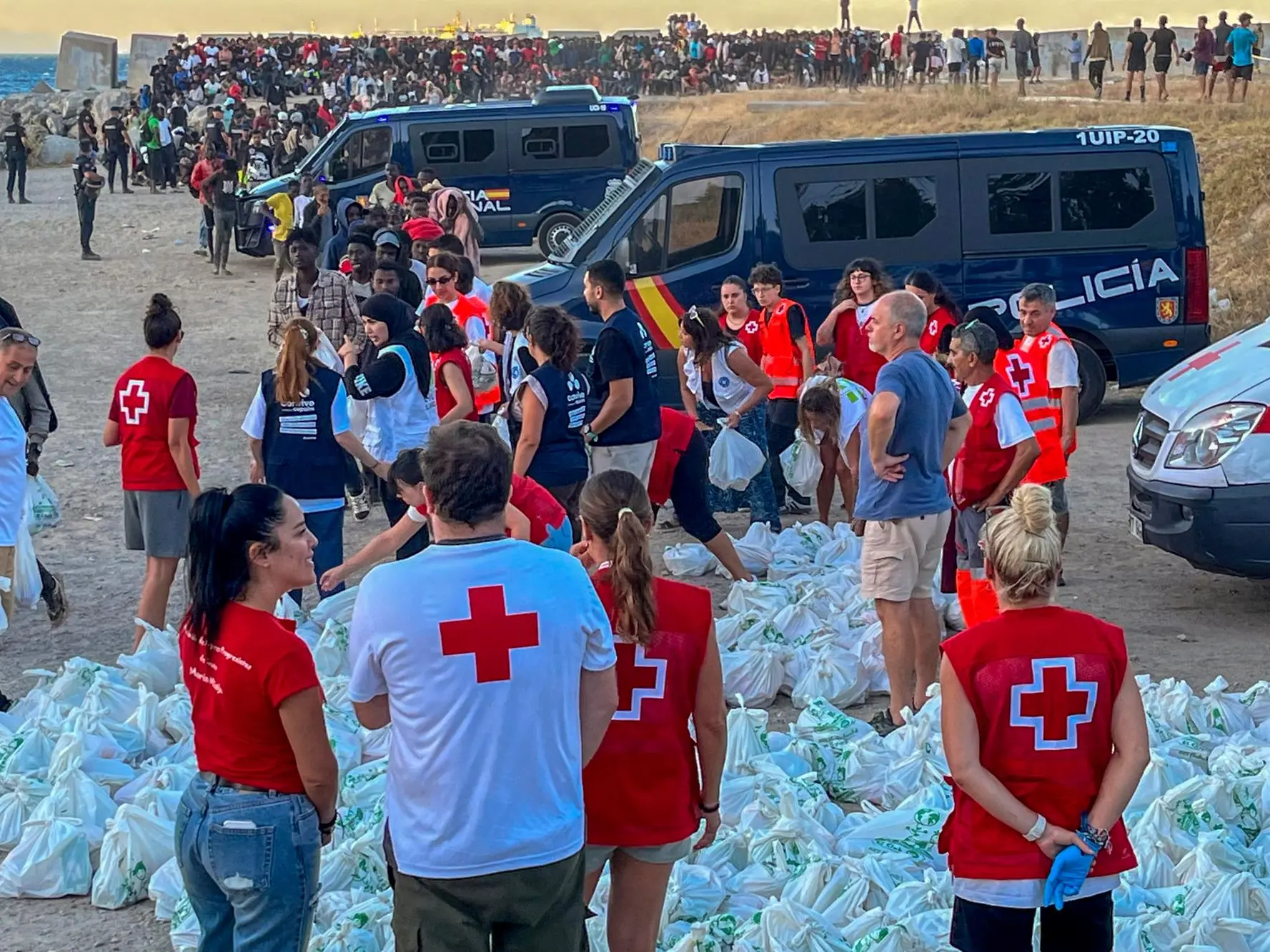 epa13150618 Red Cross personnel distribute food to migrants at El Trampolin beach in Ceuta, Spain, 04 August 2026. According to Spanish officials, around 2,500 migrants remain in Ceuta following last week's massive border rush from Morocco, with many living in overcrowded reception centers or sleeping outdoors on beaches and in parks. EPA/REDUAN