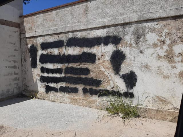 Le scritte cancellate sul muro del cimitero (foto L'Unione Sarda)