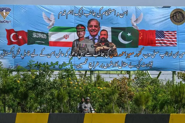 Motorcyclists ride past a billboard featuring Pakistan's Prime Minister Shehbaz Sharif (C) and Army Chief and Field Marshal Syed Asim Munir (L) in Islamabad on April 20, 2026 ahead of anticipated US-Iran peace talks. Iran insisted it has no plan to attend a new round of negotiations with the United States on April 20, as uncertainty grows over a push to stop the Middle East war from resuming. (Photo by Asif HASSAN / AFP)