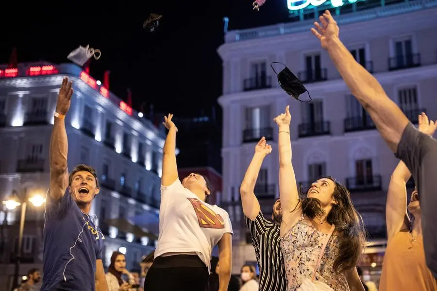 epa09302177 Youngsters throw their facial masks in the air to celebrate the end of the mandatory use of facial masks outdoors in Puerta del Sol square in Madrid, Spain, early 26 June 2021. People are allowed to go without facial masks outdoors as long as social distancing is possible. EPA/RODRIGO JIMENEZ