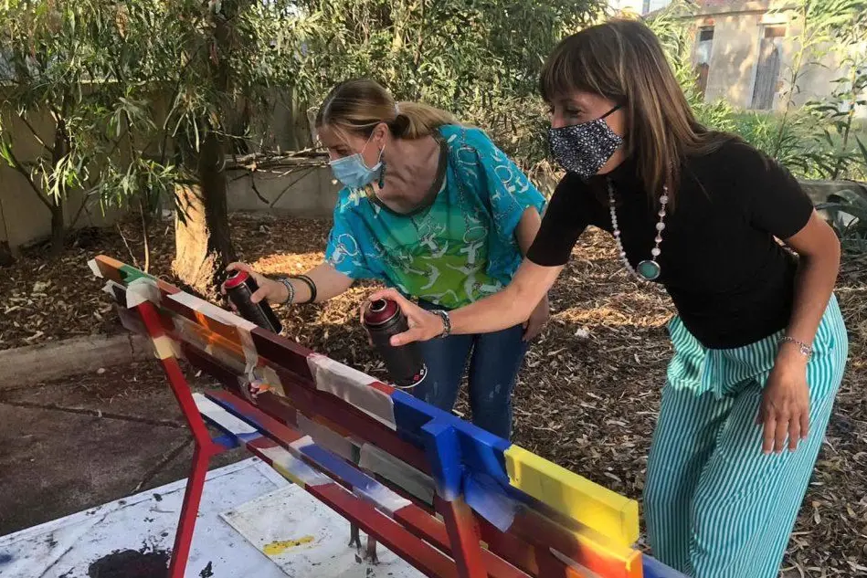Giusy Chessa (la prima da sinistra) e Silvia Mamusa mentre dipingono la panchina con i colori dell'arcobaleno (foto Pittau)