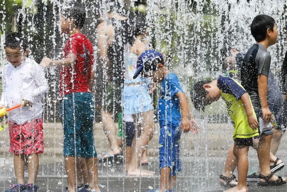 Un gruppo di bambini prova a rinfrescarsi in un parco di Tokyo