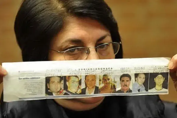 La mamma di una delle vittime mostra le immagini dei sette operai rimasti uccisi (Ansa)
