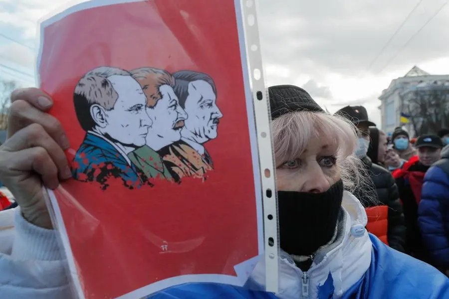 Una donna ucraina mostra un'immagine di Putin accostata a Stalin e Hitler (Ansa-Epa)