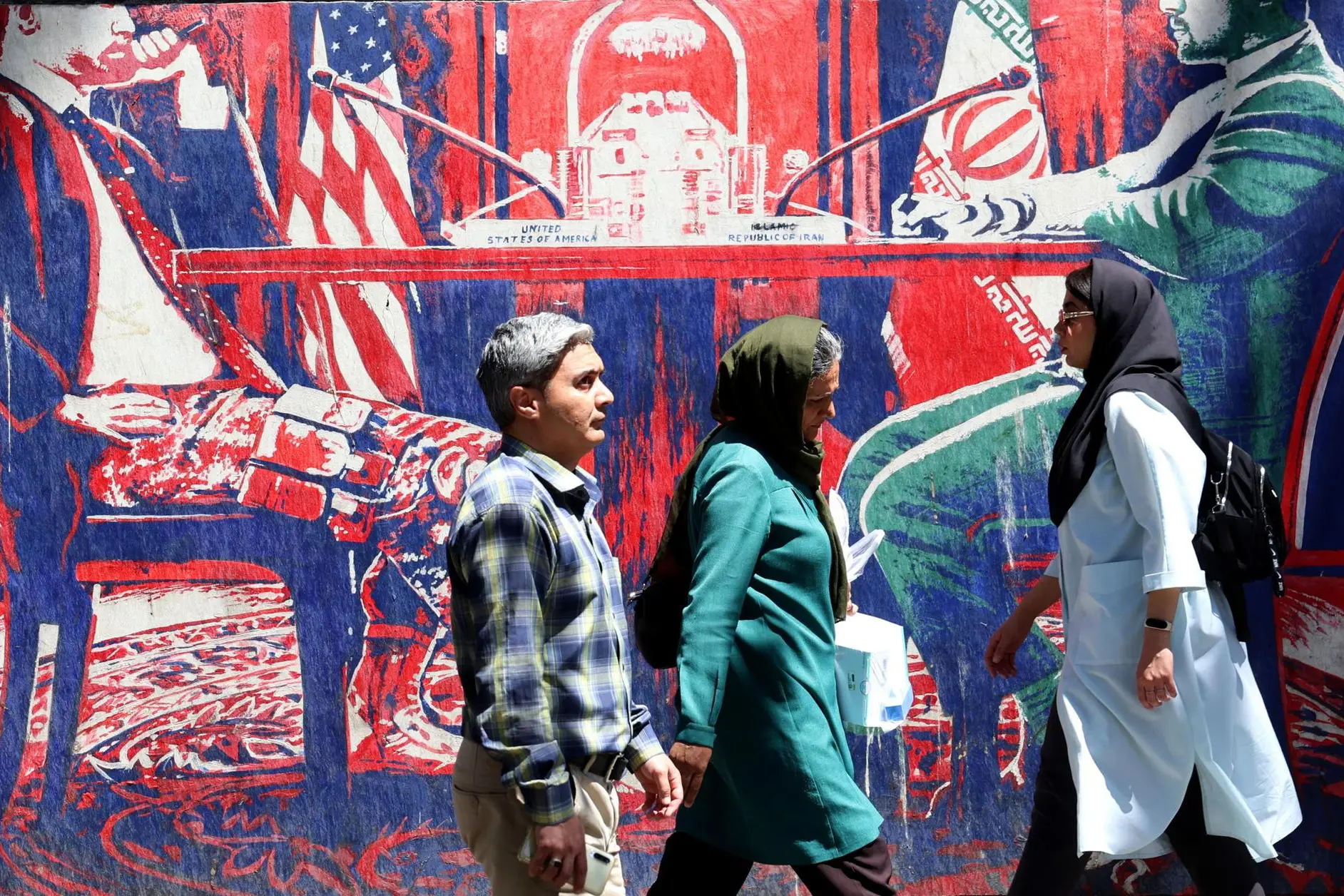 epa12994325 Iranians walk next to an anti-US mural depicting Iran and US negotiations at a table, next to the former US Embassy in Tehran in Tehran, Iran, 26 May 2026. US President Donald Trump announced that a potential peace agreement to end the conflict and reopen the Strait of Hormuz has been largely negotiated through Pakistani mediators. However, the US has launched new strikes in southern Iran. EPA/ABEDIN TAHERKENAREH
