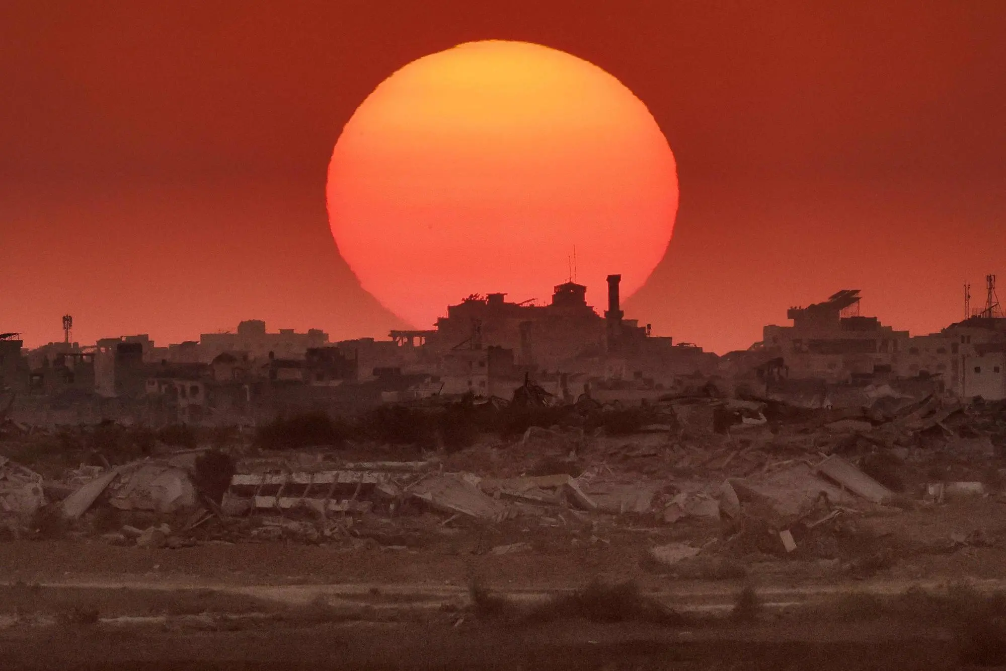 This picture taken from a position on the Israeli border with the Gaza Strip, shows the sun setting behind destroyed buildings in the besieged Palestinian territory on August 19, 2025. Gaza's civil defence agency reported that 31 people were killed on August 19 by Israeli strikes and fire across the territory, with spokesman Mahmud Bassal telling AFP the situation was "very dangerous and unbearable" in the Zeitoun and Sabra neighbourhoods of Gaza City, where he said "artillery shelling continues intermittently". (Photo by Jack GUEZ / AFP)