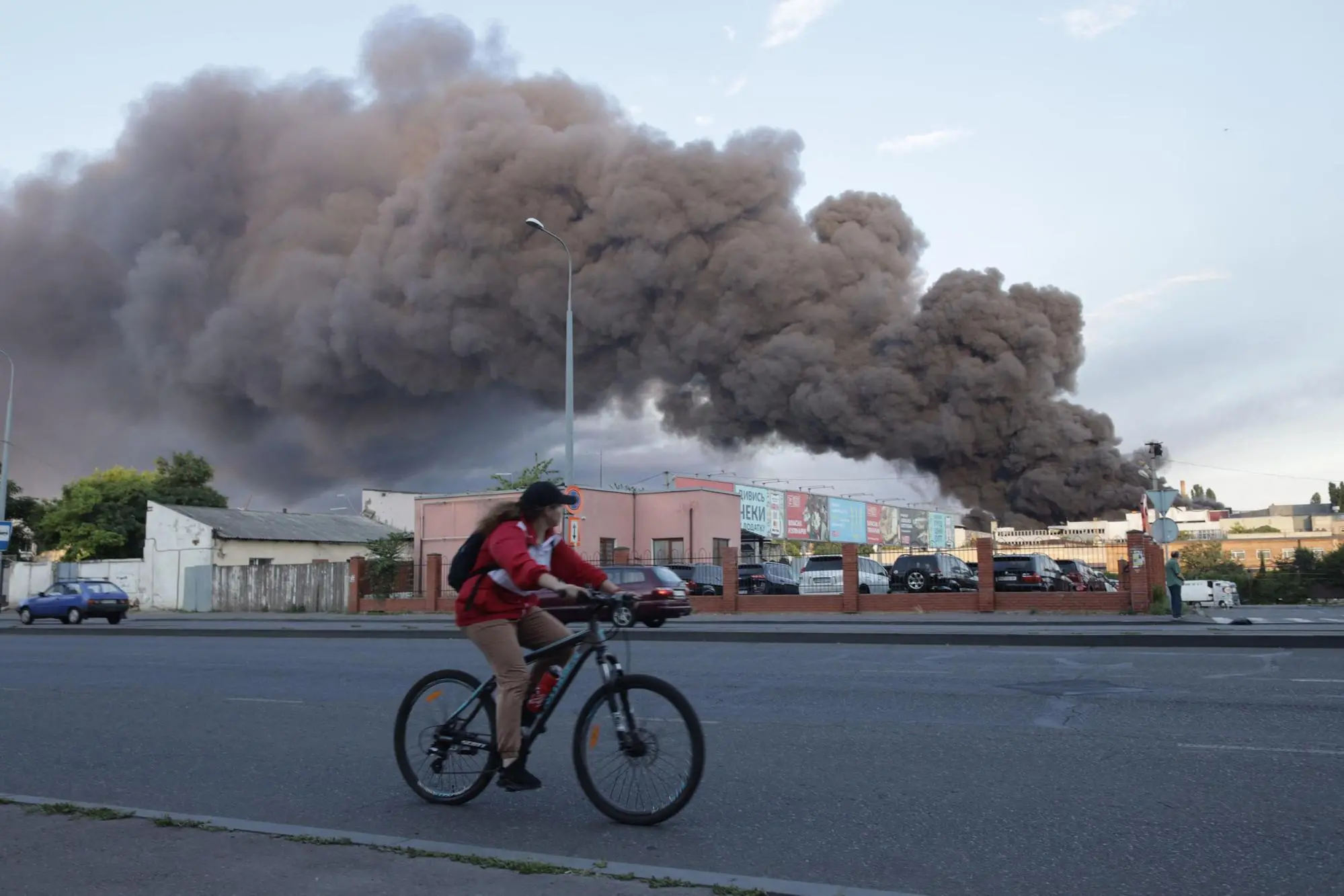 TOPSHOT - A woman riding a bicycle drives past a cloud of smoke from a fire in the background after a missile strike on a warehouse of an industrial and trading company in Odessa on July 16, 2022, amid the Russian invasion of Ukraine. (Photo by Oleksandr GIMANOV / AFP)
