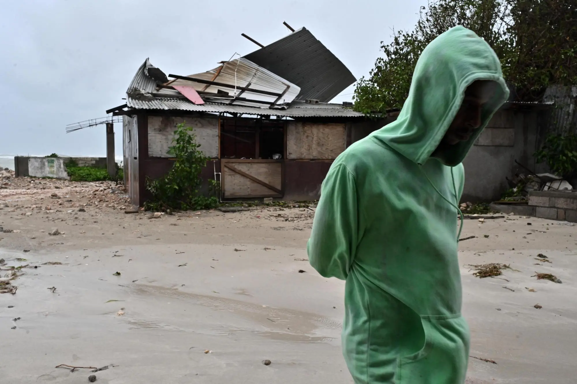 epaselect epa12486754 A man walks by a house damaged by the preliminary winds of Hurricane Melissa at Hellshire Fishing Beach in Portmore, Jamaica, 27 October 2025. Jamaican Prime Minister Andrew Holness said the government has a multifaceted plan to ensure a 'swift and effective' response to the storm