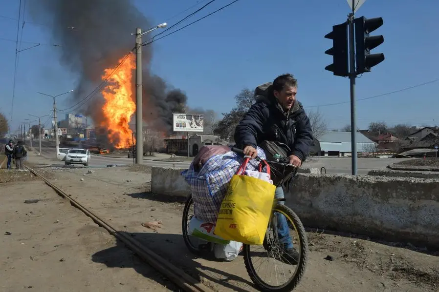 A man carries a bicycle with his belongings as fire engulfs a gas station following an artillery attack on the 30th day of the Russian invasion of Ukraine in the northeastern city of Kharkiv on March 25, 2022. - Russian strikes targeting a medical facility in Ukraine's second city of Kharkiv on March 25, 2022, killing at least four civilians and wounding several others, Ukrainian officials said. (Photo by Sergey BOBOK / AFP)