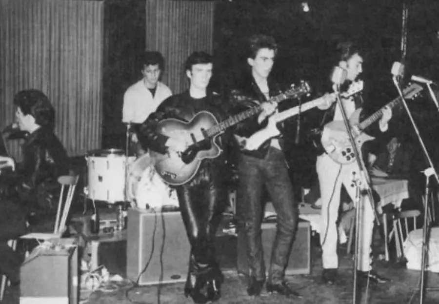 Stuart Sutcliffe (al centro, col basso) sul palco insieme ai Beatles (da Wikipedia)