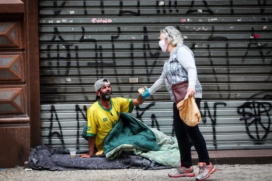 Una donna dà un pezzo di pane a un homeless a San Paolo (Ansa)