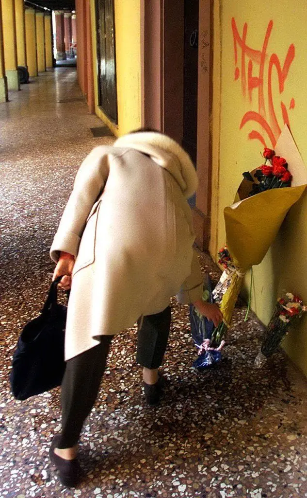Una donna lascia dei fiori a terra, dove è morto Marco Biagi