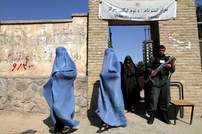 epa04100798 An armed Afghan policeman stands guard as burqa-clad Afghan women leave a voters registration center, in Herat, Afghanistan, 26 February 2014. Afghanistan's presidential election campaign kicked off on 02 February with security concerns heightened after the killing of two aides of one of the 11 candidates. The preparations for the presidential elections in Afghanistan since then have been repeatedly interfereed and threatened by suspected Taliban insurgents. EPA/JALIL REZAYEE