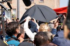 Emmanuel Macron protetto da un ombrello dai lanci di pomodori a Cergy-Pontoise, alla sua prima uscita dopo la rielezione (foto Afp)