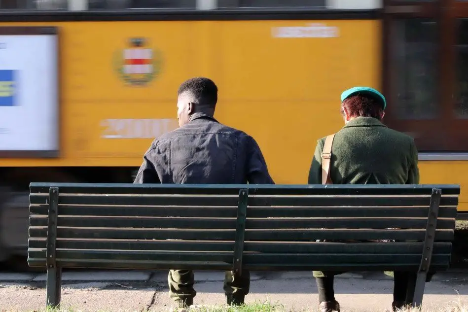 Due persone alla fermata del tram a Milano (Ansa)