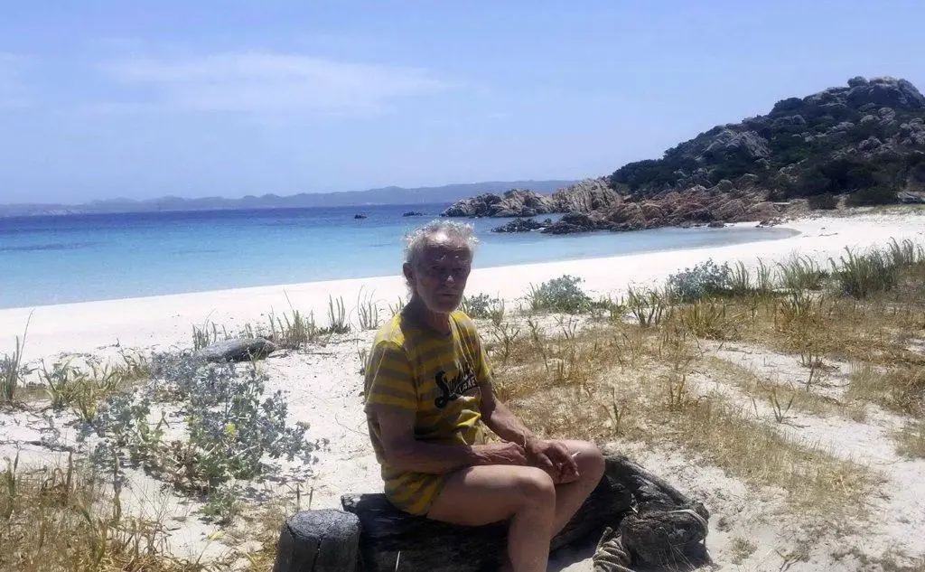 Mauro Morandi seduto su un tronco, alle sue spalle il mare (Ansa)