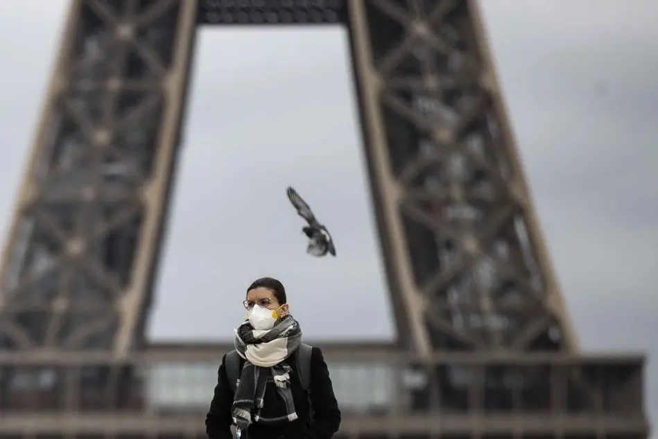 Una donna con la mascherina davanti alla Tour Eiffel (Ansa)