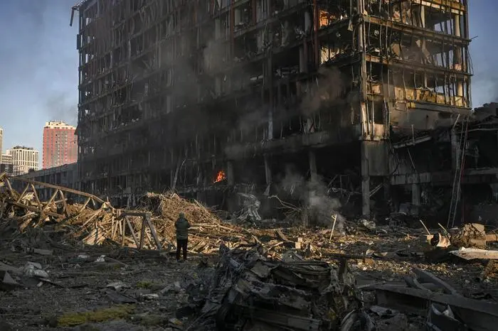 A man stand looking at the burning and destroyed Retroville shopping mall after a Russian attack on the northwest of the capital Kyiv on March 21, 2022. - At least six people were killed in the overnight bombing of a shopping centre in the Ukrainian capital Kyiv, an AFP journalist said, with rescuers combing the wreckage for other victims. The 10-storey building was hit by a powerful blast that pulverised vehicles in its car park and left a crater several metres (yards) wide. (Photo by ARIS MESSINIS / AFP)