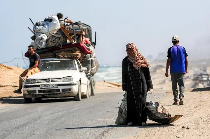 TOPSHOT - A woman walks pulling a sack in one hand and a scrap metal sheet used as a container for other items in the other, along the coastal road used by people evacuating southbound from Gaza City, in Nuseirat in the central Gaza Strip, on September 9, 2025. Israel has been intensifying its bombardment of Gaza City in preparation for its military operation, despite repeated entreaties from Western nations and aid agencies to stop. (Photo by Eyad BABA / AFP)