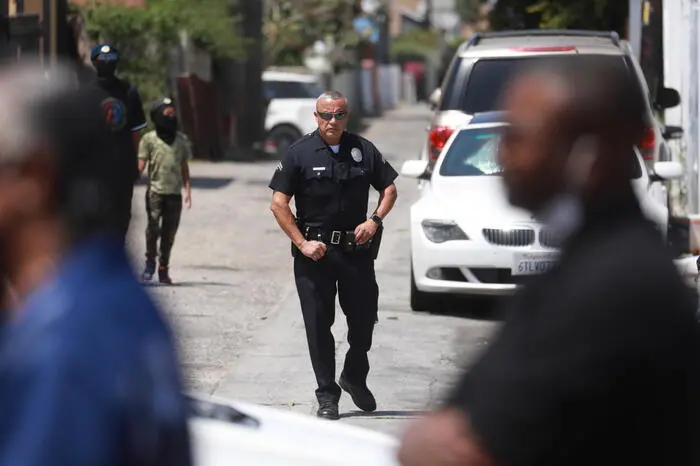 epa09917569 An LAPD officer watches people gather at the intersection of Florence and Normandie Avenues, as the 30th Anniversary of the Los Angeles Riots is remembered in Los Angeles, California, USA, 29 April 2022. Over 60 people are thought to have been killed and hundreds of businesses destroyed after four white police officers were aquitted in 1992 for beating Rodney King in Los Angeles on 03 March 1991. This intersection was the flashpoint after the acquittal of LAPD police officers shown in a videotaped beating of black motorist Rodney King. EPA/DAVID SWANSON
