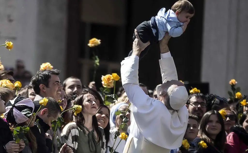 John Malkovich nei panni del Papa mentre solleva un bimbo in piazza San Pietro
