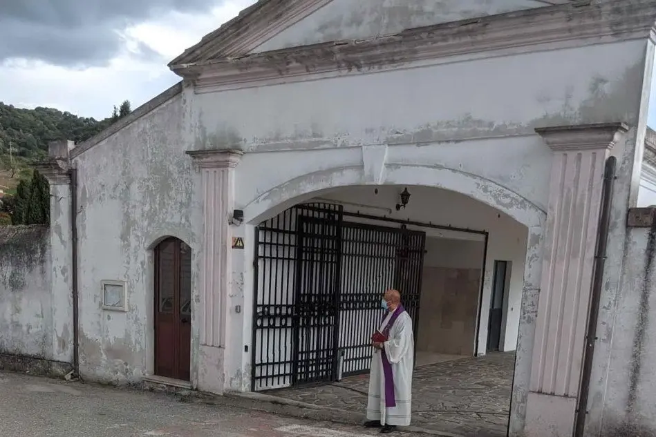 Il sacerdote aspetta all'ingresso del cimitero di Benetutti l'arrivo della salma (foto Tellini)