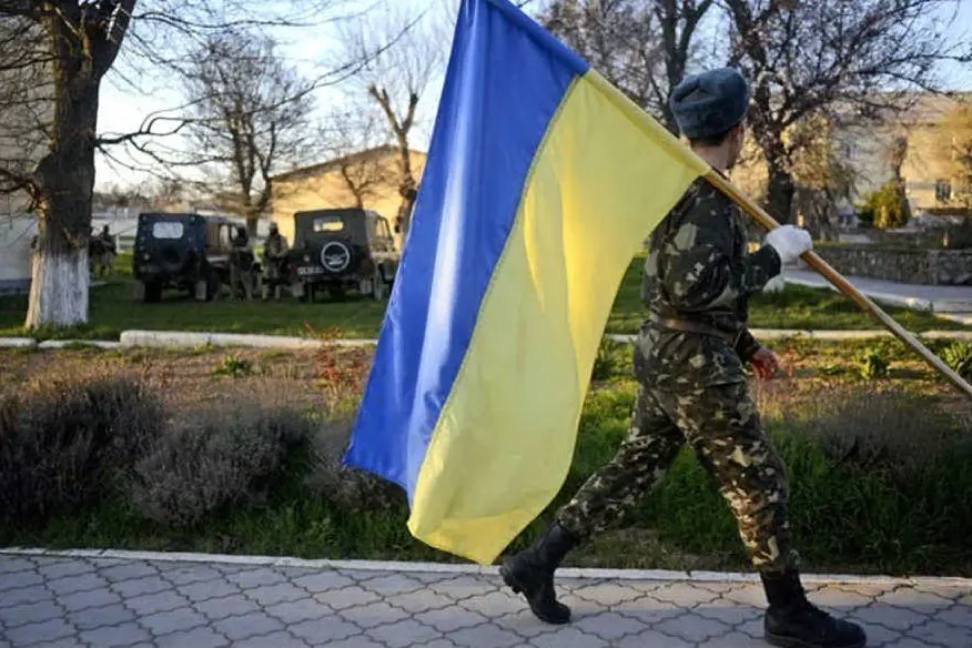 Un soldato ucraino lascia una base in Crimea portando via la bandiera nazionale