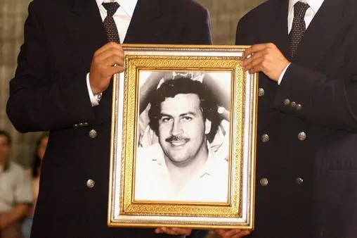 Two unidentified men carry the potrait of late Colombian drug trafficker Pablo Escobar Gaviria during a mass in commemoration for the 10th anniversary of Escobar's death held at Jardines Montesacro cemetery, south of Medellin, on Sunday 30 November 2003. Escobar was shot and killed by Colombian special forces on 02 December 1993 in Medellin. EPA/EDWIN BUSTAMANTE