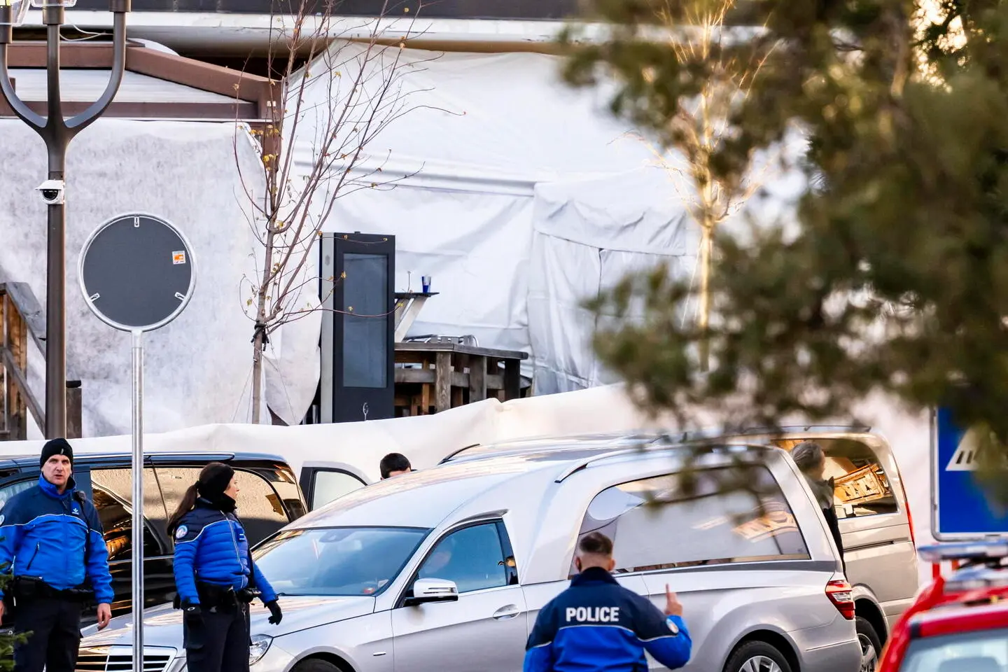 epa12620751 Police officers stand near a hearse in area where a fire broke out at the Le Constellation bar and lounge following an explosion in the early hours of New Year's Eve, in Crans-Montana, Switzerland, 01 January 2026. According to the police, several dozen people lost their lives in the fire and around one hundred people were also reported injured. EPA/JEAN-CHRISTOPHE BOTT