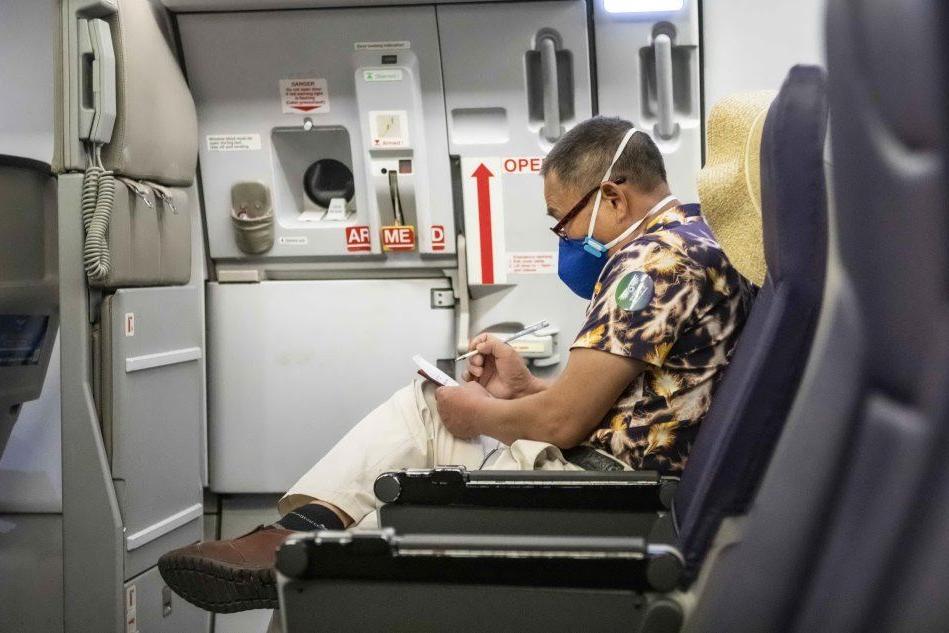 Un passeggero cinese a bordo di un aereo con la mascherina protettiva (Ansa)=
