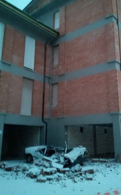 Un'auto distrutta dalle macerie cadute da un palazzo durante una scossa