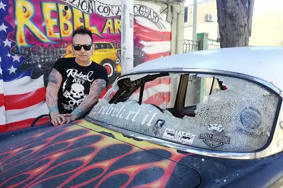 L'artista vicino a una delle auto danneggiate (foto L'Unione Sarda)