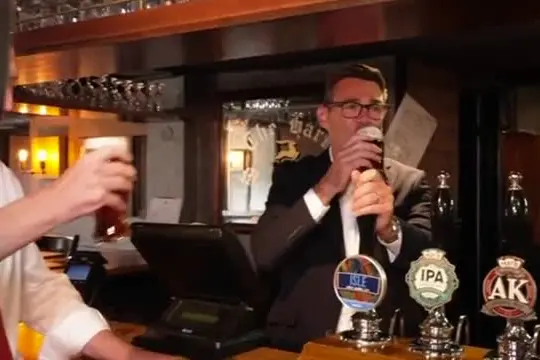 Andy Burnham festeggia il taglio delle tasse al pub con birra in mano