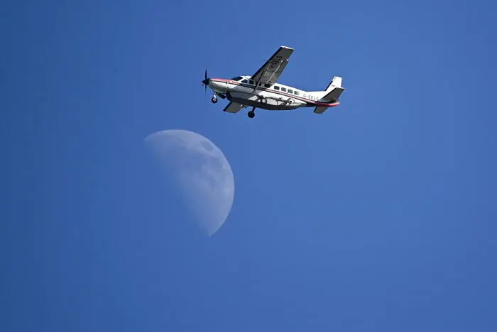 epa09351010 A Cessna 208B Grand Caravan Aircraft G-EELS fly’s past the moon over the Royal St George's golf course during the 3rd round of The Open 2021 golf championship at in Sandwich, Kent, Britain, 17 July 2021. EPA/NEIL HALL