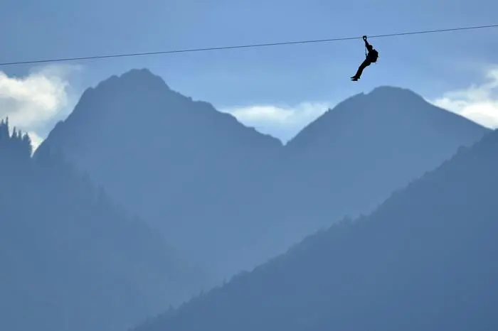 epa04428420 A man slips down the zipline before the opening of the fair 'Foire du Valais' above the town of Martigny, Switzerland, 02 October 2014. The Zipline is made of 1'123 meters of cable; it takes one minute 10 to slip down, passes an altitude of 120 meters and a speeds of up to 85 km. According the organizer of the fair the Zipline driving through a town of 18,000 inhabitants, should be unique in the world. EPA/MAXIME SCHMID
