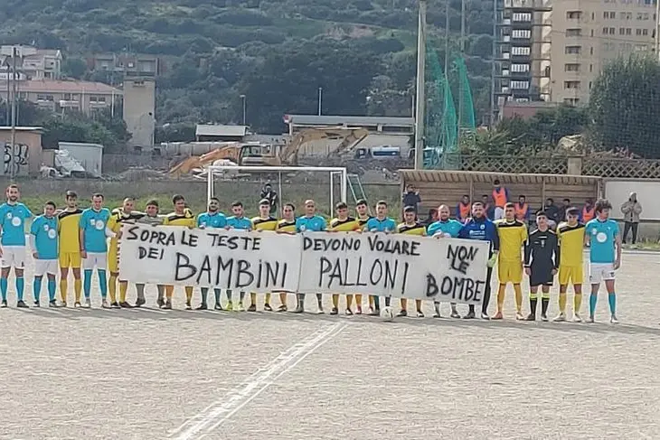 I giocatori di Giovent&ugrave; Assemini e Isuledda con lo striscione esposto prima della gara (foto Paolo Melis)