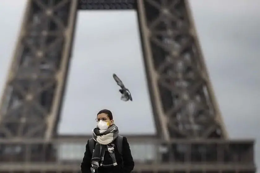 Una donna con la mascherina davanti alla Tour Eiffel (archivio L'Unione Sarda)