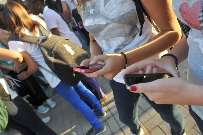 Adolescenti alle prese con gli smartphone prima di entrare a scuola (Ansa)