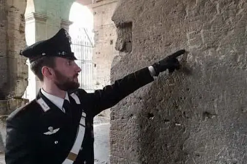 Un carabiniere mostra le iniziali incise nel muro (foto da twitter)