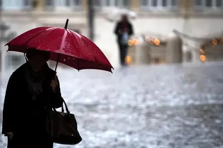 Una persona si ripara con l'ombrello sotto la pioggia in piazza Colonna a Roma, 15 dicembre 2017. ANSA/ANGELO CARCONI