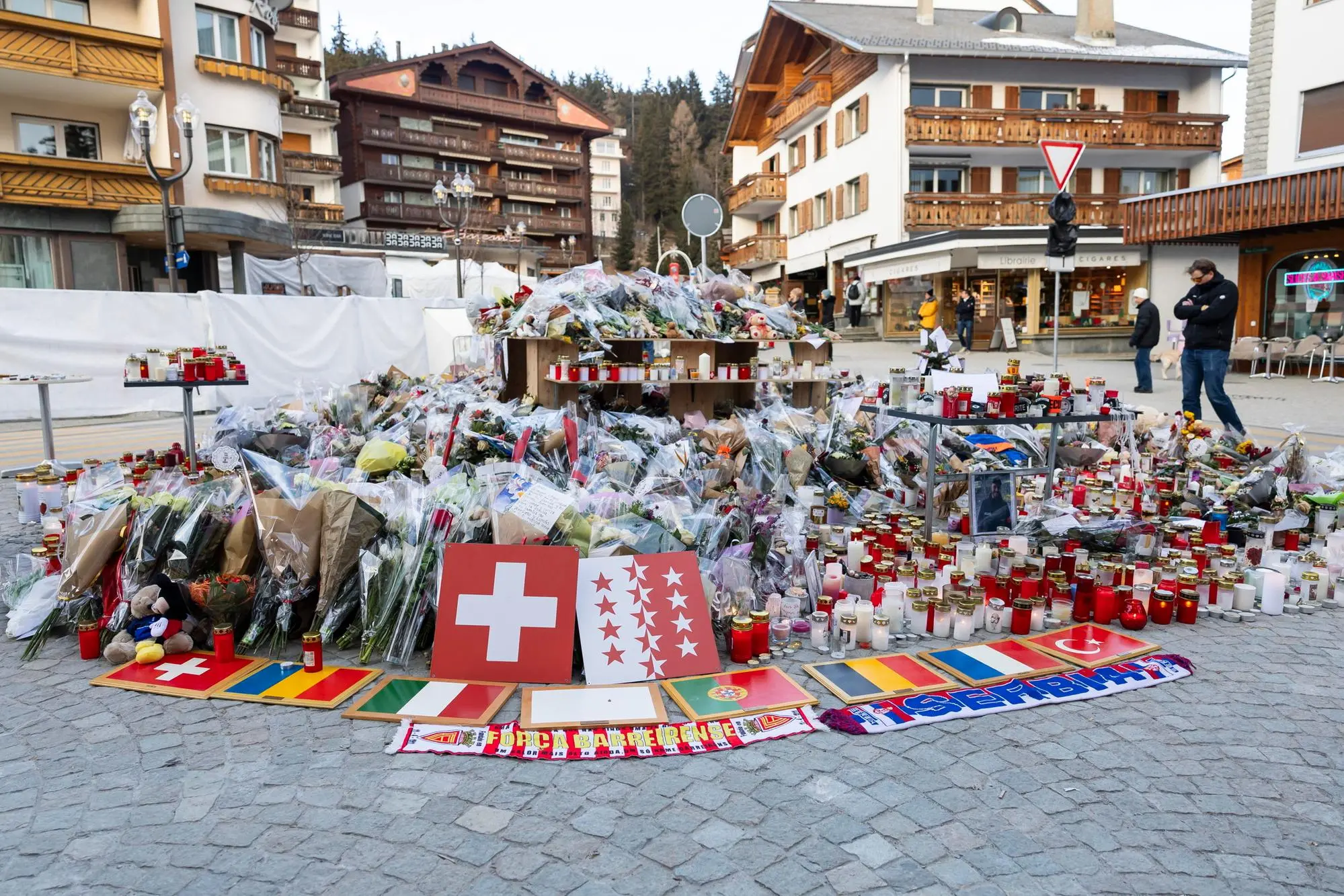 Plaques bearing flags representing Switzerland, Romania, Italy, Portugal, Belgium, France, and Turkey were placed along with flowers and candles in tribute to the victims after the fire at the 'Le Constellation' bar and lounge, in Crans-Montana