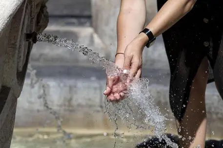 Un ragazza si bagna le mani per proteggersi dal forte caldo (Ansa)