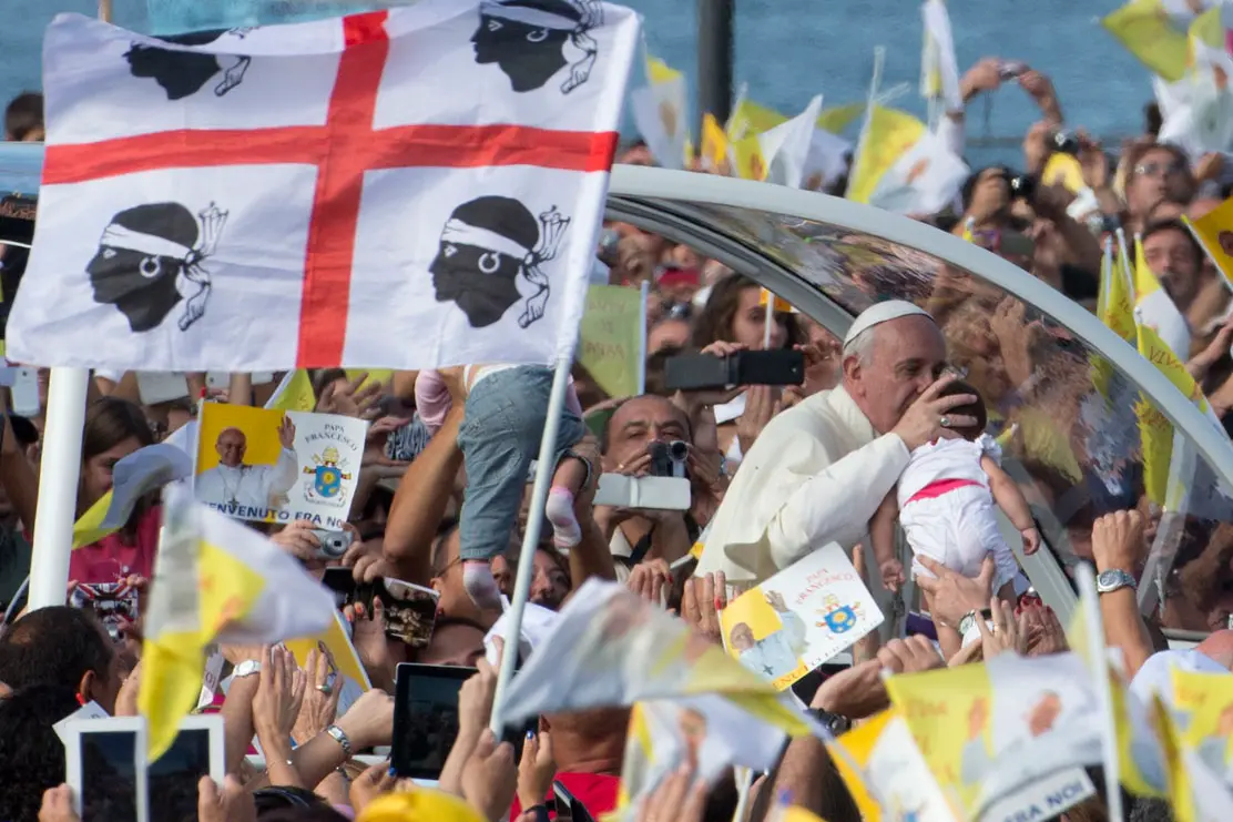 Papa Francesco bacia un bimbo sulla Papa mobile durante la visita a Cagliari nel 2013 (Foto simbolo)