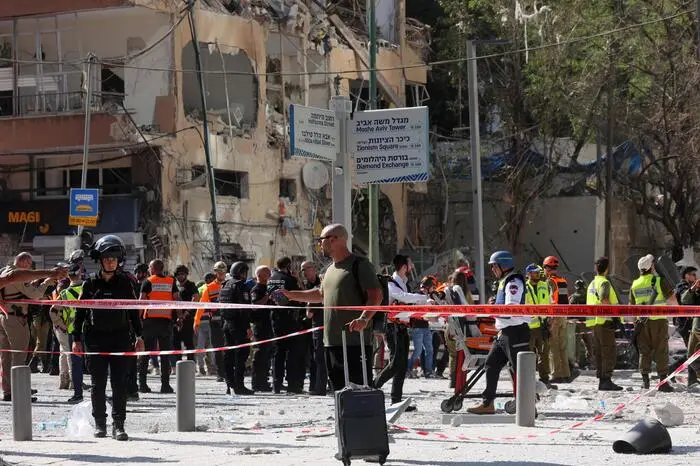 A man walks with a suitcase past first responders gathering outside a heavily-damaged building at the site of an Iranian missile attack in Ramat Gan in central Israel near Tel Aviv, on June 19, 2025. A hospital in southern Israel was hit during a barrage of "dozens" of Iranian missiles on June 19, officials said, while another impact was reported by emergency services in the Tel Aviv area. (Photo by GIL COHEN-MAGEN / AFP)