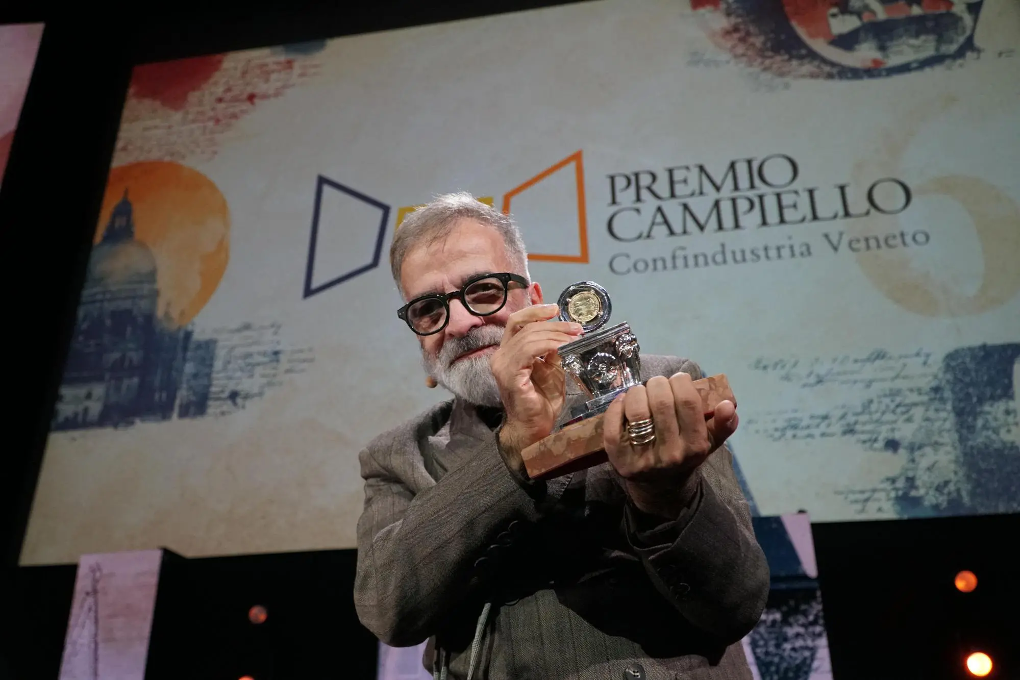 Lo scrittore Marcello Fois, vincitore della 64° edizione del Premio Letterario Campiello con “L’Immensa distrazione” (Einaudi) posa sul palco reggendo con le mani l’ambito premio, al termine della cerimonia finale, nella sala grande del Palazzo del Cinema del Lido, Venezia 3 ottobre 2026. ANSA/ANDREA MEROLA ------ Writer Marcello Fois, winner of the 64th edition of the Campiello Literary Prize for *L’Immensa distrazione* (Einaudi), poses on stage holding the coveted award at the end of the final ceremony in the main hall of the Palazzo del Cinema at the Lido, Venice, October 3, 2026. ANSA/ANDREA MEROLA