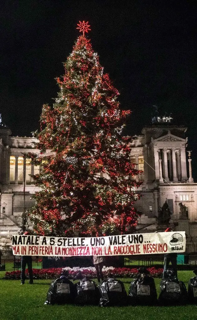 Rifiuti sotto l'Albero di Natale in piazza Venezia (portati da alcuni cittadini delle periferie) e uno striscione contro la Raggi (Ansa)