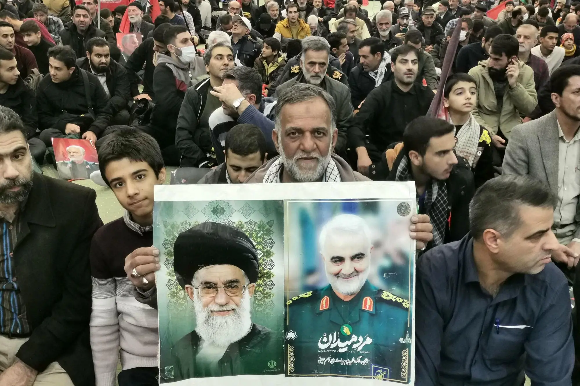 Un uomo in Iran mostra i ritratti di Ali Khamenei e Soleimani (Ansa)